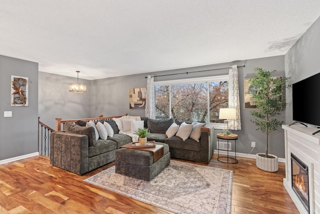 living area featuring an inviting chandelier, baseboards, a glass covered fireplace, and wood finished floors