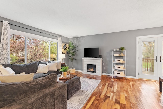 living area with baseboards, a glass covered fireplace, and wood finished floors