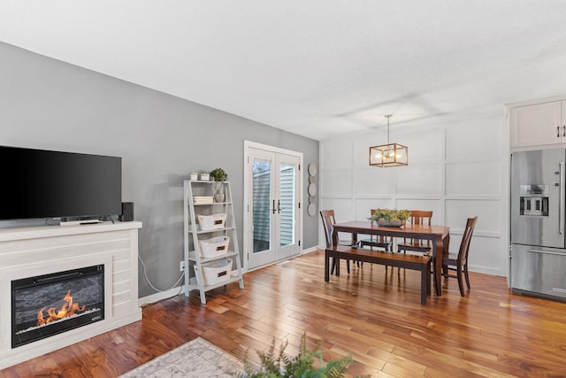 dining area with a glass covered fireplace, wood finished floors, an inviting chandelier, and a decorative wall