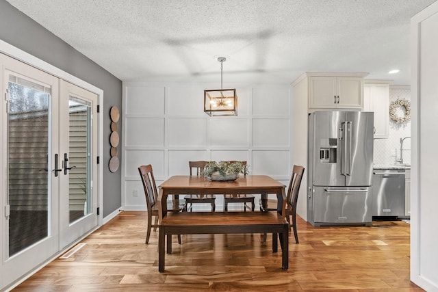 dining space with light wood-style floors, a textured ceiling, a decorative wall, and a chandelier