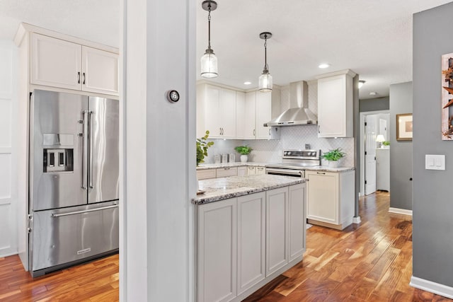 kitchen with wall chimney range hood, appliances with stainless steel finishes, backsplash, and light wood finished floors