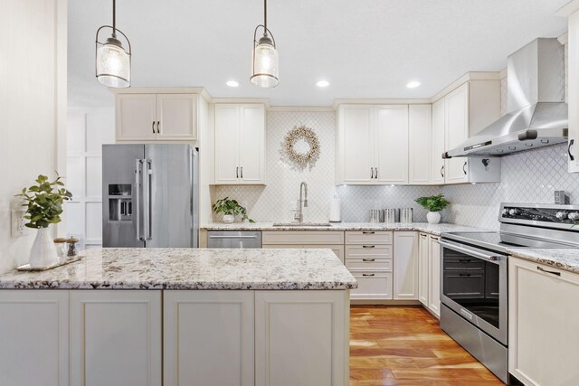 kitchen featuring wall chimney range hood, light wood-type flooring, tasteful backsplash, a sink, and stainless steel appliances