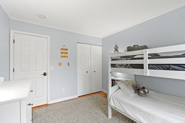 bedroom with baseboards, ornamental molding, a closet, and wood finished floors