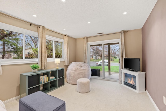 sitting room featuring recessed lighting, carpet flooring, and a glass covered fireplace