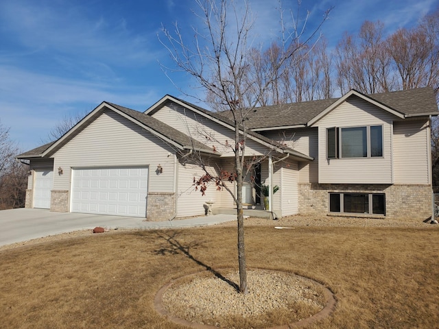 split level home featuring brick siding, a front yard, roof with shingles, driveway, and an attached garage