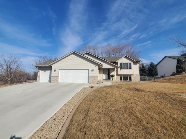 tri-level home with a front yard, fence, driveway, a garage, and brick siding