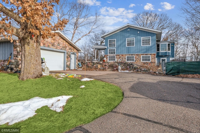 view of front of property featuring aphalt driveway, stone siding, and a front yard