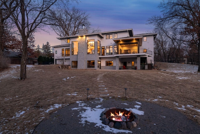 snow covered rear of property featuring a balcony, a chimney, and a fire pit