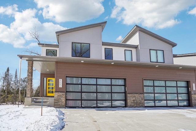 modern home with stone siding, an attached garage, and stucco siding