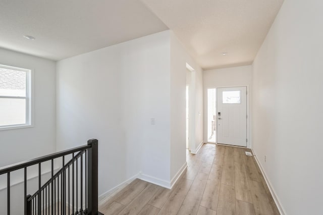 hallway featuring light wood finished floors, baseboards, and an upstairs landing