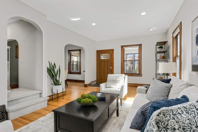 living room featuring recessed lighting, baseboards, arched walkways, and light wood-style flooring