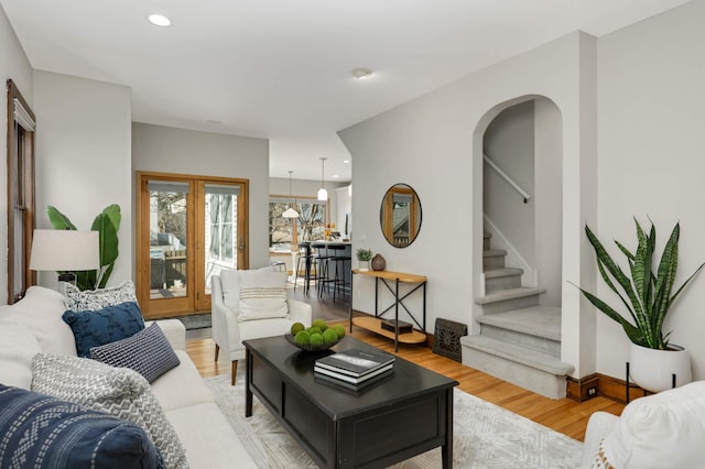 living room with recessed lighting, arched walkways, light wood-style floors, baseboards, and stairs