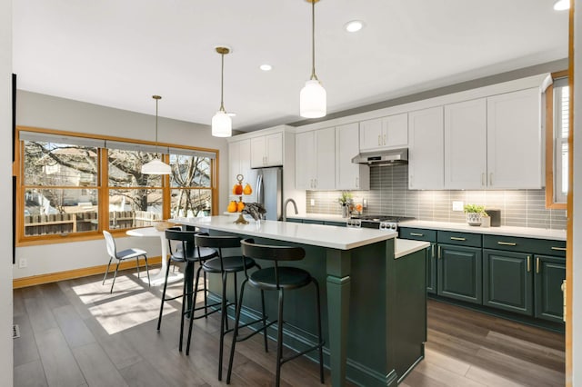 kitchen featuring freestanding refrigerator, light countertops, tasteful backsplash, and under cabinet range hood