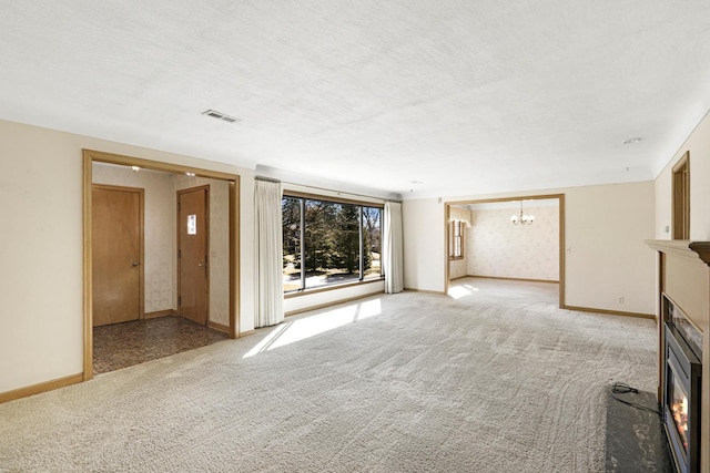 unfurnished living room with a glass covered fireplace, light colored carpet, visible vents, and baseboards