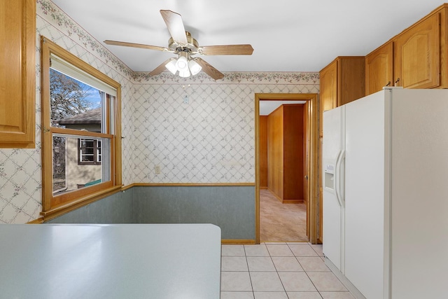 kitchen with light tile patterned floors, wallpapered walls, ceiling fan, white refrigerator with ice dispenser, and brown cabinets