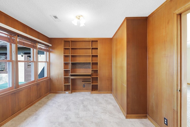 unfurnished room with built in features, visible vents, wood walls, and a textured ceiling