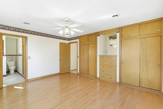 unfurnished bedroom featuring visible vents, multiple closets, ensuite bathroom, and light wood finished floors