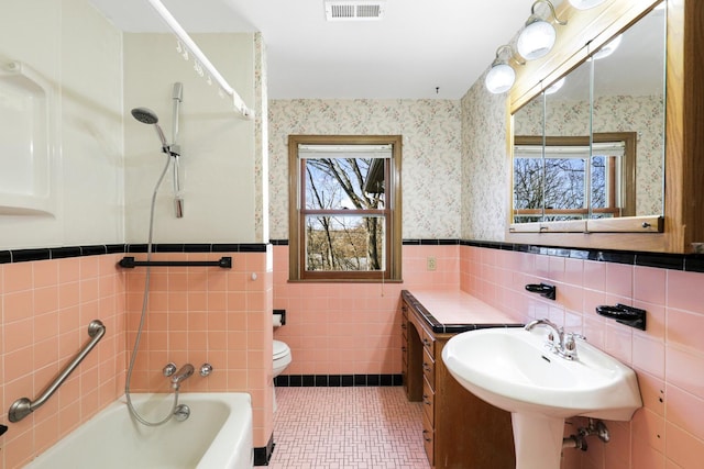 bathroom featuring visible vents, wallpapered walls, wainscoting, walk in shower, and a bathtub