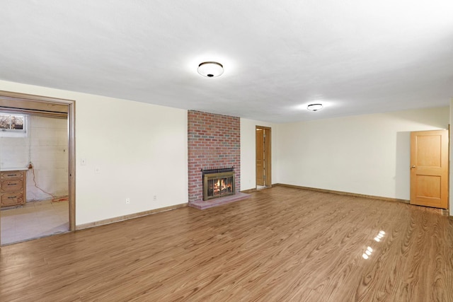 unfurnished living room featuring a brick fireplace, light wood-style floors, and baseboards