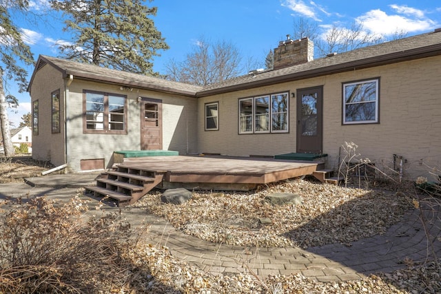 rear view of house featuring brick siding, a wooden deck, and a chimney