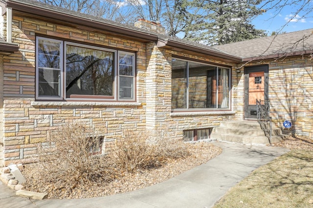 view of side of property featuring stone siding, roof with shingles, and a chimney