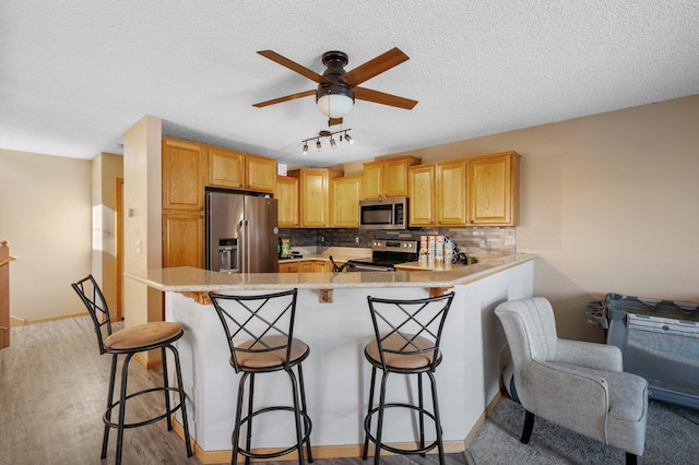 kitchen featuring a textured ceiling, stainless steel appliances, kitchen peninsula, a breakfast bar area, and tasteful backsplash