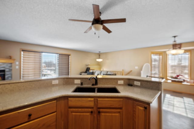 kitchen with a fireplace, decorative light fixtures, sink, ceiling fan, and a textured ceiling