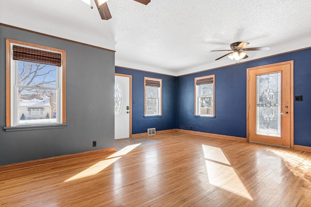 unfurnished living room with light wood-type flooring, visible vents, a ceiling fan, and baseboards