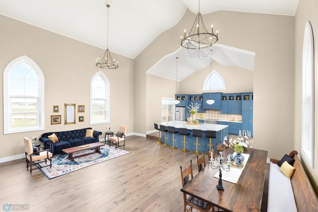 living area with a chandelier, high vaulted ceiling, baseboards, and wood finished floors