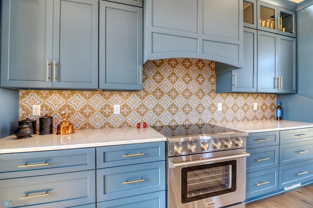 kitchen featuring glass insert cabinets, high end stainless steel range oven, light countertops, blue cabinetry, and backsplash