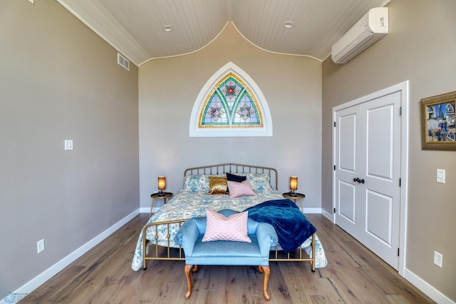 bedroom featuring an AC wall unit, visible vents, baseboards, and wood finished floors