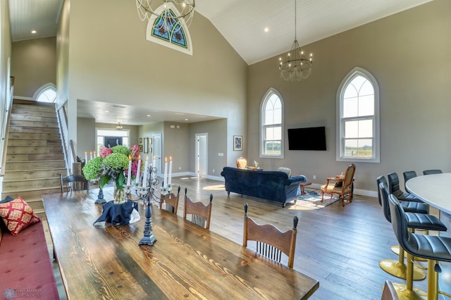 dining area featuring high vaulted ceiling, baseboards, stairs, hardwood / wood-style floors, and an inviting chandelier