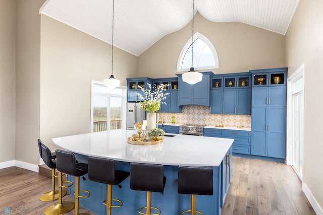 kitchen with blue cabinets, light wood-type flooring, a center island with sink, and light countertops