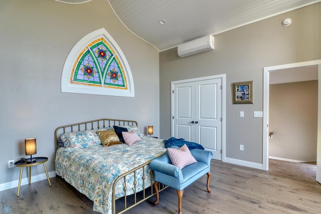 bedroom featuring a closet, baseboards, an AC wall unit, and wood finished floors