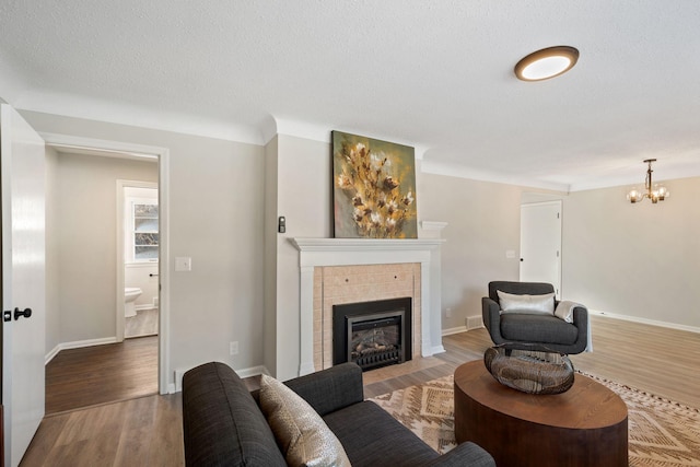 living area with a textured ceiling, wood finished floors, baseboards, a tiled fireplace, and an inviting chandelier