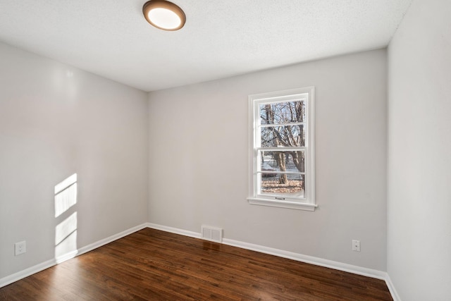 empty room with dark wood-type flooring, visible vents, and baseboards