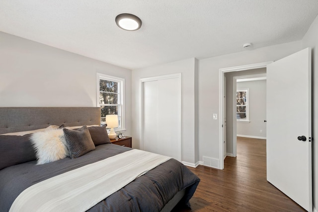 bedroom with dark wood-type flooring, a closet, multiple windows, and baseboards