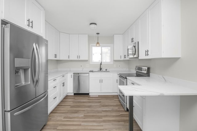 kitchen featuring appliances with stainless steel finishes, hanging light fixtures, light stone counters, sink, and white cabinetry