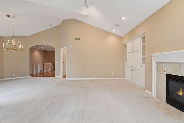 unfurnished living room featuring a chandelier, light carpet, a tile fireplace, and arched walkways