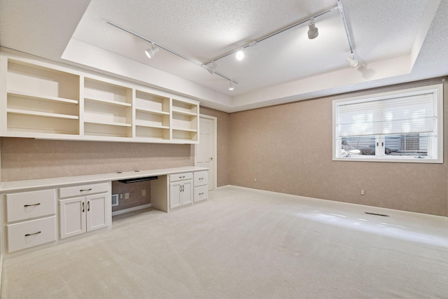 unfurnished office with light carpet, built in desk, a textured ceiling, and track lighting