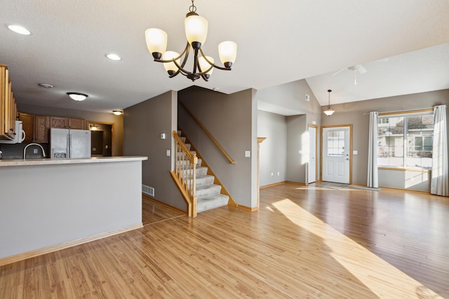 unfurnished living room with light wood finished floors, visible vents, stairway, lofted ceiling, and a sink