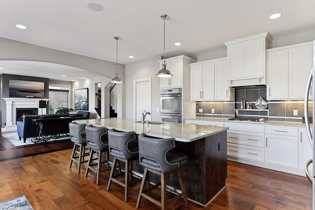 221 George St, Excelsior, MN 55331 - kitchen with stainless steel appliances, arched walkways, decorative backsplash, a sink, and white cabinets
