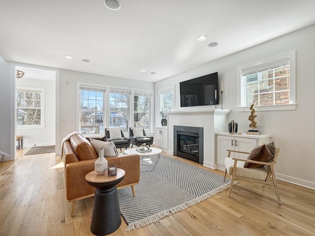 living area featuring plenty of natural light, light wood-type flooring, a fireplace with flush hearth, and baseboards