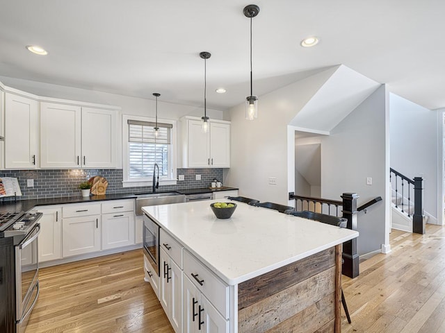 kitchen featuring stainless steel stove, white cabinetry, hanging light fixtures, and a sink