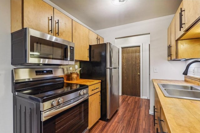 kitchen featuring stainless steel appliances, a sink, light countertops, dark wood-style floors, and brown cabinetry