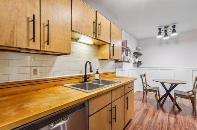 kitchen featuring dark wood finished floors, stainless steel dishwasher, brown cabinetry, wainscoting, and a sink