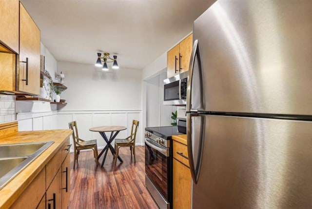 kitchen featuring dark wood-style flooring, appliances with stainless steel finishes, brown cabinetry, wainscoting, and a sink