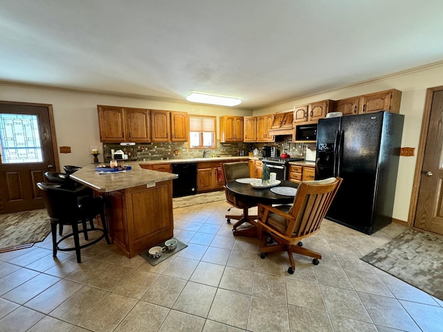 kitchen featuring brown cabinets, light countertops, decorative backsplash, black appliances, and a kitchen breakfast bar