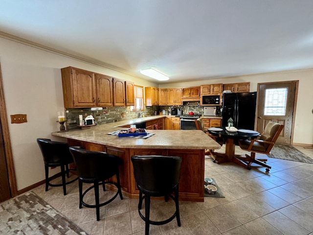 kitchen with a peninsula, black appliances, brown cabinets, and light countertops