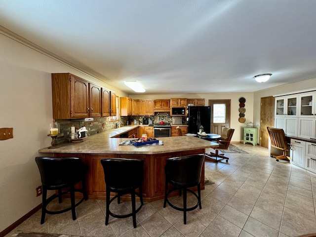 kitchen featuring a peninsula, a breakfast bar, black appliances, tasteful backsplash, and brown cabinetry